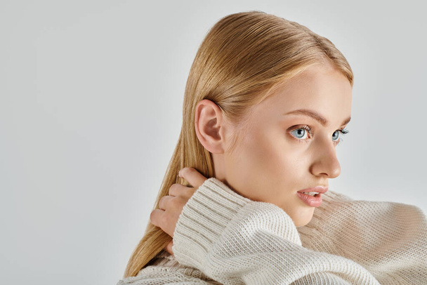 donna ipnotizzante in maglione bianco lavorato a maglia e trucco naturale toccando i capelli biondi su grigio, ritratto - Foto, immagini