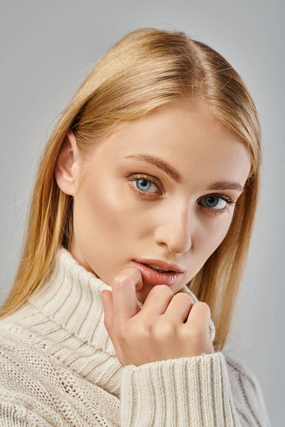 Nahaufnahme Porträt einer jungen Blondine im Winterpullover mit blonden Haaren und natürlichem Make-up auf grau - Foto, Bild