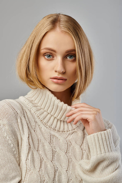 atraktivní žena s přírodním make-upem a blond vlasy na sobě bílý pletený svetr na šedé, portrét - Fotografie, Obrázek