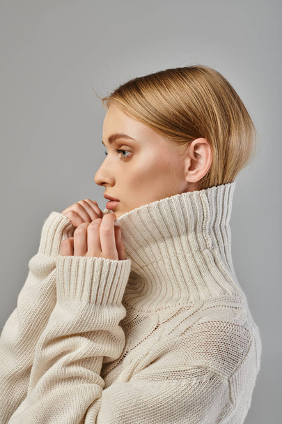 profilo ritratto di donna bionda in maglione bianco lavorato a maglia con collo alto su grigio, stile invernale - Foto, immagini