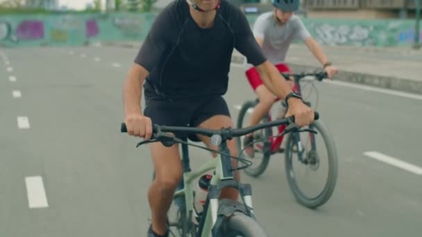 Elülső nézet billenő lefelé lövés a férfi és a fiú sisakot lovaglás kerékpárok felé kamera a városi úton - Felvétel, videó