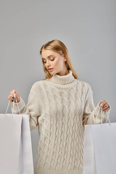 暖かいスタイリッシュなセーターで魅力的なブロンドの女性,灰色のホワイトショッピングバッグ,季節のショッピング - 写真・画像