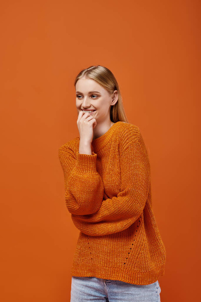 улыбающаяся блондинка в ярком вязаном свитере улыбается и смотрит в сторону оранжевых, зимних эмоций - Фото, изображение