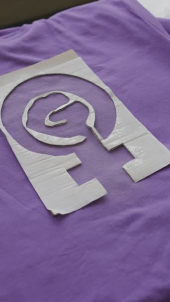 Никаких людей сверху с картонным трафаретом с феминистским символом на фиолетовой хлопчатобумажной футболке - Кадры, видео