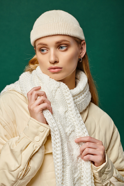 donna pensosa in giacca calda e sciarpa bianca con cappello beanie su sfondo verde, moda invernale - Foto, immagini