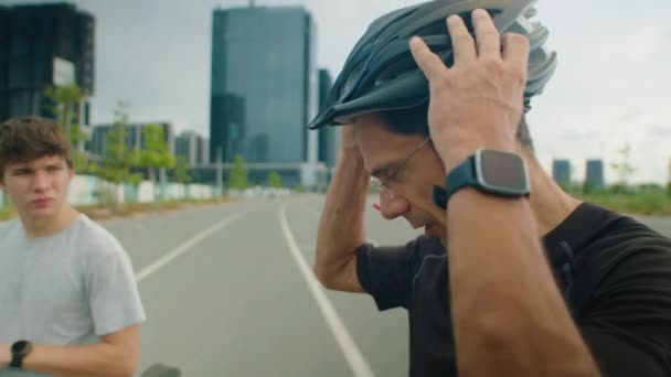 Tirador medio de hombre que se pone el casco de ciclismo mientras se prepara para montar en bicicleta con su hijo - Metraje, vídeo