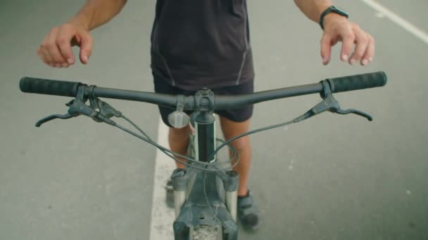Καλλιεργημένη βολή του αρσενικού ποδηλάτη στα αθλητικά κρατώντας τιμόνι, ενώ πρόκειται να οδηγούν ποδήλατο σε εξωτερικούς χώρους - Πλάνα, βίντεο