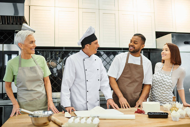 chef allegro guardando i suoi studenti diversi, mentre insegnando loro come cuocere, corsi di cucina - Foto, immagini