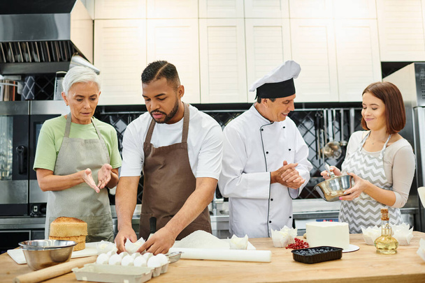 Reifer, fröhlicher Konditor mit weißem Hut, umgeben von seinen vielfältigen Schülern während des Kochkurses - Foto, Bild