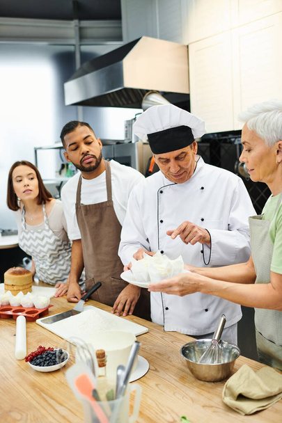 komea konsentroitu kokki valkoisessa hatussa selittää, miten leipoa eri opiskelijoille, makeiset - Valokuva, kuva