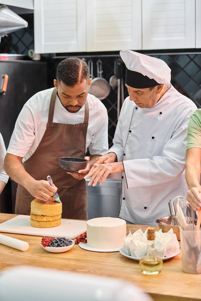 зрілий шеф-кухар в білому капелюсі навчає свого афроамериканського студента, як використовувати силіконову щітку на торт - Фото, зображення