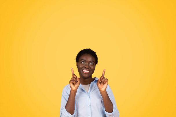 Улыбающаяся молодая африканская студентка-американка в случайных точках указывает пальцем на пространство для копирования, наслаждается уроком, изолированным на жёлтом фоне студии. Обучение и образование, продажа внимания - Фото, изображение