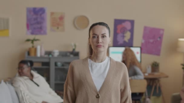 Medium-Slowmo-Porträt einer jungen selbstbewussten kaukasischen Feminismus-Aktivistin, die mit gefalteten Händen in einer modernen Wohnung steht, während sie sich mit anderen Frauen beim feministischen Clubtreffen trifft - Filmmaterial, Video