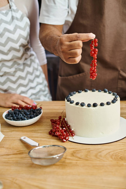cropped view of young african american man decorating cake with berries next to his friend - Photo, Image