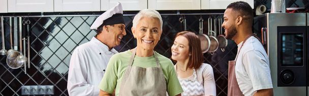 zaměření na ženu s dort s úsměvem na kameru s rozmazané rozmanité přátele a kuchař na pozadí, banner - Fotografie, Obrázek