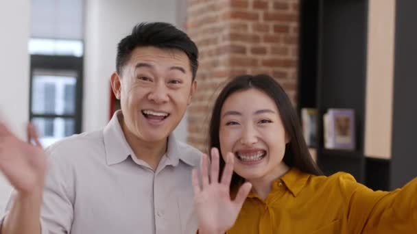 Rodinný blog. Šťastný asijský ženatý muž a žena nahrávání video zprávy na smartphone na sociální média, stojí spolu doma interiéru, kamera pov portrét - Záběry, video