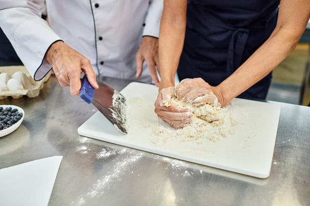 cropped view of mature woman working with dough with chief cook helping her, confectionary - Photo, Image