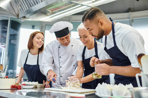 alegres chefs multirraciais em aventais trabalhando com massa junto com seu cozinheiro chefe, confeitaria - Foto, Imagem