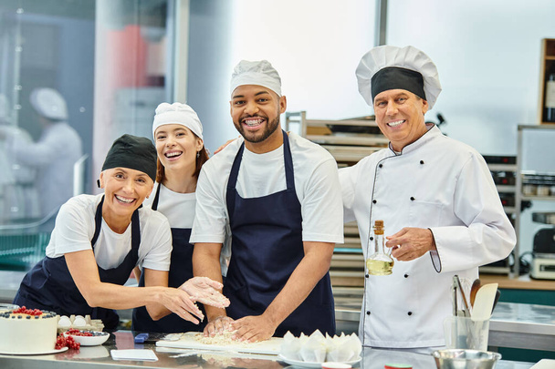 fröhliche multikulturelle Köche und Chefköche in Hauben lächeln in die Kamera, während sie mit Teig arbeiten - Foto, Bild