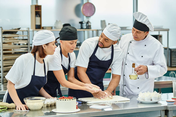 chef multiculturali che lavorano con la pasta insieme accanto al capo cuoco con olio, dolciumi - Foto, immagini