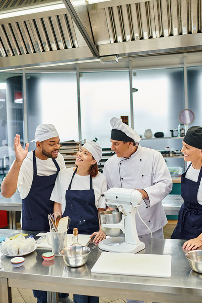 веселий афроамериканський шеф-кухар піднімає руку, щоб поставити питання поруч зі своїми колегами і головним кухарем - Фото, зображення