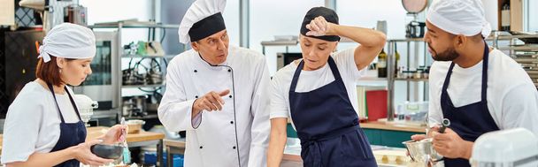 dojrzały szef kuchni w białym kapeluszu wyjaśniając, jak piec do jego wielorasowe ciężko pracujących kucharzy, sztandar - Zdjęcie, obraz