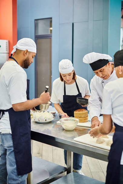 мультикультурная команда поваров в фартуках и токах, работающих над выпечкой вместе с шеф-поваром - Фото, изображение