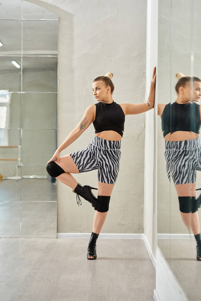 mujer de moda en pantalones cortos de cebra y top balances negros en una pierna mientras baila contra el espejo - Foto, Imagen