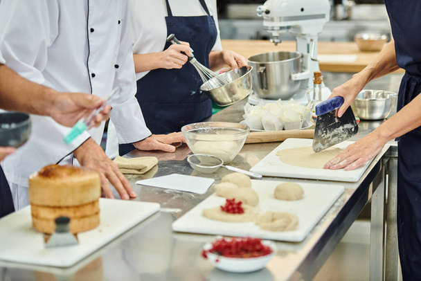 ostříhaný pohled na tvrdě pracující kuchaře a kuchaře pracující s těstem na kuchyni, cukrovinky - Fotografie, Obrázek