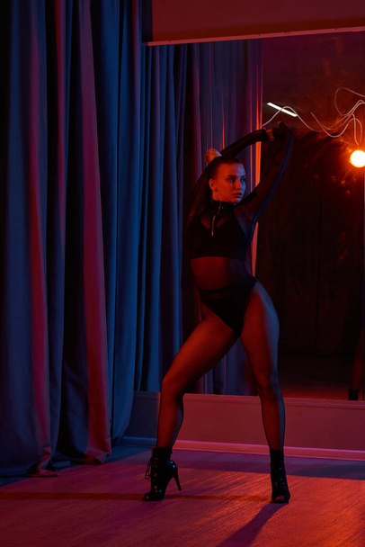 Een sierlijke danseres slaat een pose in haar zwarte maillot en visnet panty, omlijst door gordijn - Foto, afbeelding