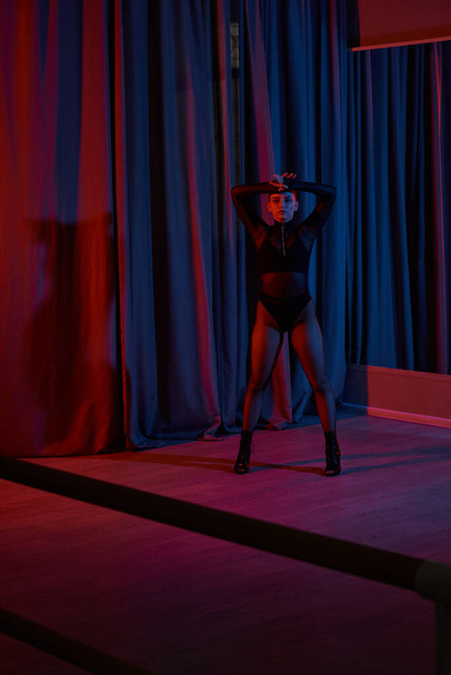 mujer en medias de rejilla y tacones altos golpea una pose elegante cerca de la cortina durante el rendimiento - Foto, imagen