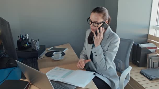 Μεσαία αργή λήψη του Καυκάσου γυναίκα των επιχειρήσεων αναθεώρηση οικονομική έκθεση, ενώ απαντώντας τηλεφώνημα και στη συνέχεια πληκτρολογώντας στο φορητό υπολογιστή - Πλάνα, βίντεο