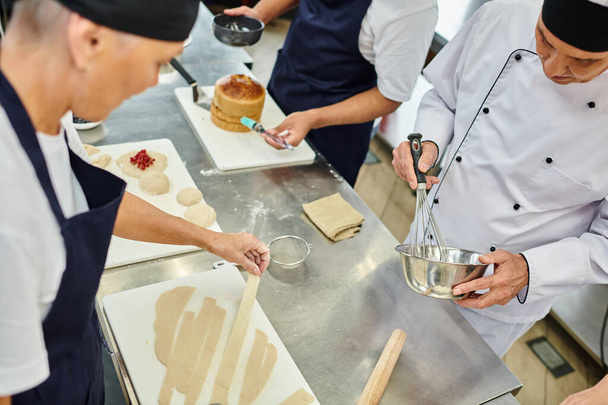 goed uitziende multiraciale koks in schorten werken samen met deeg op keuken, zoetwaren - Foto, afbeelding