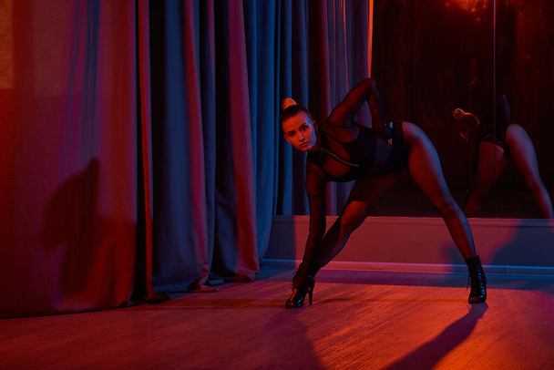 χαριτωμένη γυναίκα ετοιμάζεται να πάρει τη σκηνή, μαύρο κορμάκι της και ψηλά τακούνια αντανακλώντας στον καθρέφτη - Φωτογραφία, εικόνα