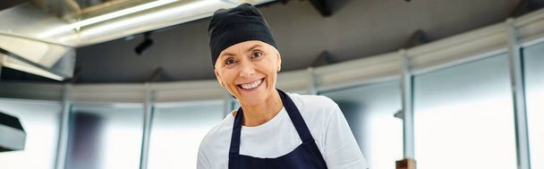 hermosa mujer madura chef en toque azul y delantal sonriendo a la cámara, confitería, pancarta - Foto, Imagen