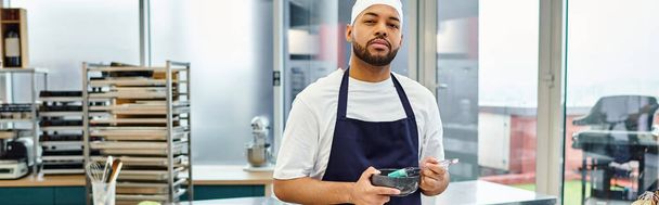 gutaussehender afrikanisch-amerikanischer Koch in Haube, der in die Kamera schaut, während er Küche, Süßwaren, Banner - Foto, Bild
