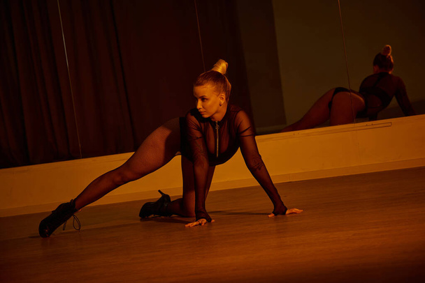 bailarina alcanza una pose mientras muestra su equilibrio y fluidez en un maillot negro y tacones altos - Foto, imagen