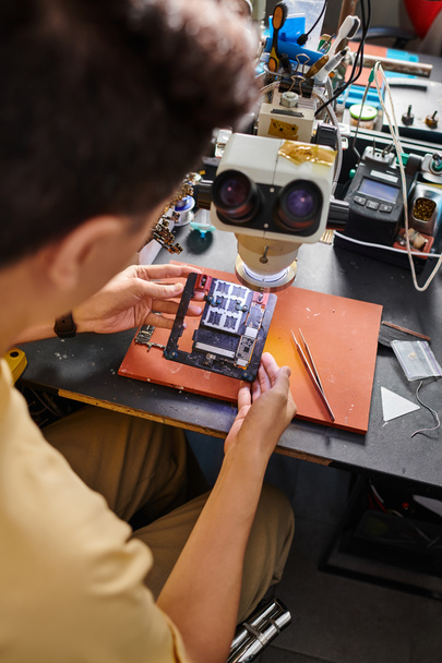 verschwommener Reparateur betrachtet Mikroschema moderner elektronischer Geräte am Arbeitsplatz in der Werkstatt - Foto, Bild