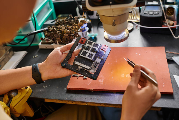 Ausgeschnittene Ansicht eines professionellen Technikers, der in der Reparaturwerkstatt einen Satz elektronischer Geräte untersucht - Foto, Bild