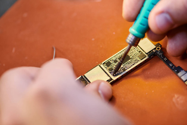 close-up zicht op bijgesneden technicus monteren chipset door solderen in reparatiewerkplaats, kleine bedrijven - Foto, afbeelding