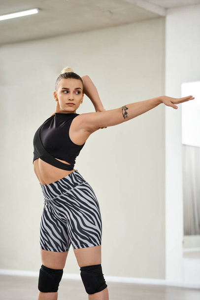 Eine anmutige Tänzerin streckt ihren Körper und ihre Arme in lebhaften Zebra-Shorts und einem schwarzen Oberteil, Flexibilität - Foto, Bild