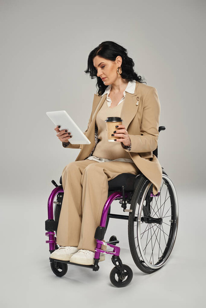 belle femme handicapée en tenue chic pastel en fauteuil roulant regardant la tablette et tenant du café - Photo, image