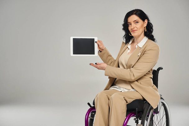 車椅子に座ってカメラでタブレットを見せるエレガントなスーツの魅力的な障害のある女性 - 写真・画像