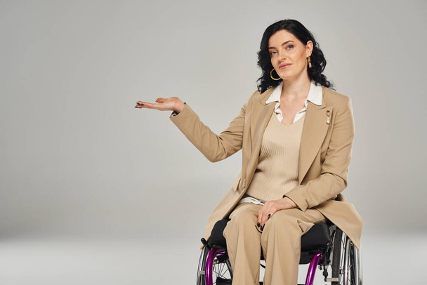 mulher bonita com deficiência em cadeira de rodas em pastel terno gestos e olhando para a câmera - Foto, Imagem