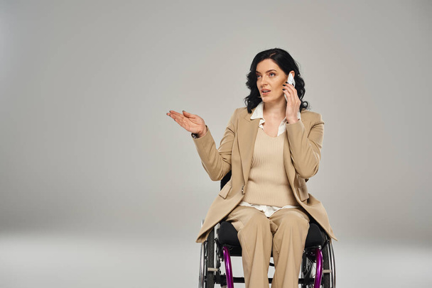 mujer discapacitada de buen aspecto en traje pastel en silla de ruedas hablando por teléfono móvil - Foto, Imagen