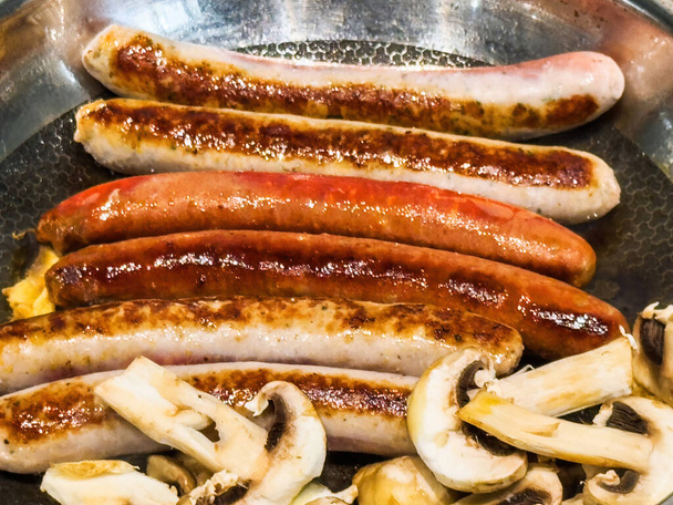 Крупним планом макро знімок ковбас і грибів-чемпіонів, що стирчать на сковороді - Фото, зображення