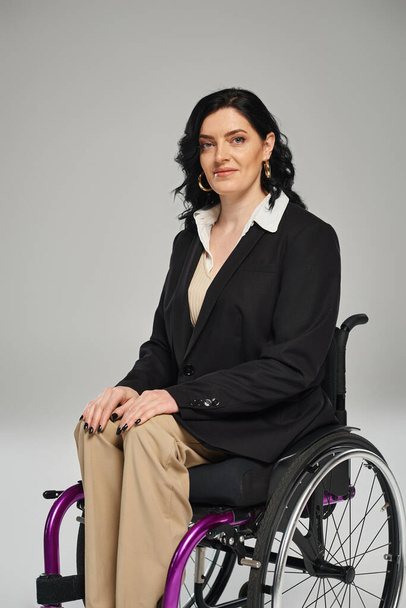 весела приваблива жінка з обмеженими можливостями в чорному шикарному блістері, сидячи в інвалідному візку і посміхаючись на камеру - Фото, зображення
