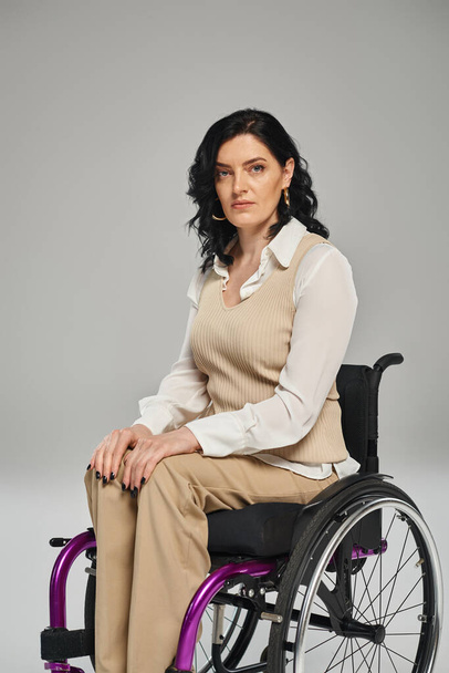 aantrekkelijke brunette gehandicapte vrouw in pastel chique kleding in rolstoel kijken recht op camera - Foto, afbeelding