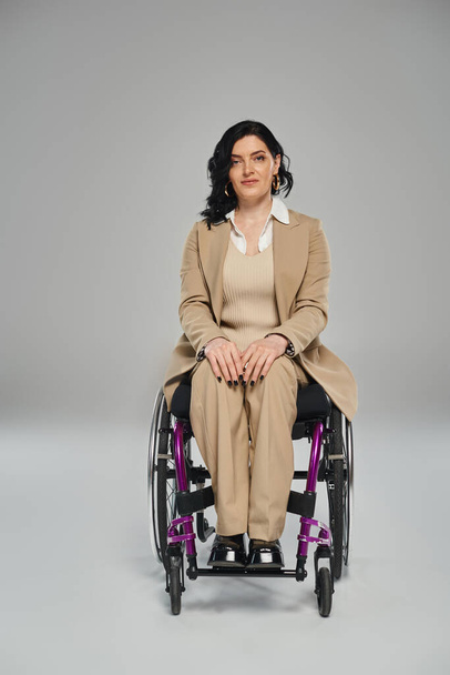 confident woman with mobility disability in chic suit sitting in wheelchair and looking at camera - Photo, Image