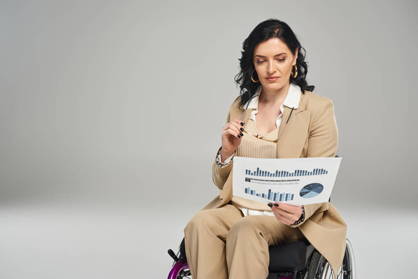 mujer guapa con discapacidad en silla de ruedas sosteniendo sus gafas y mirando sus gráficos - Foto, Imagen
